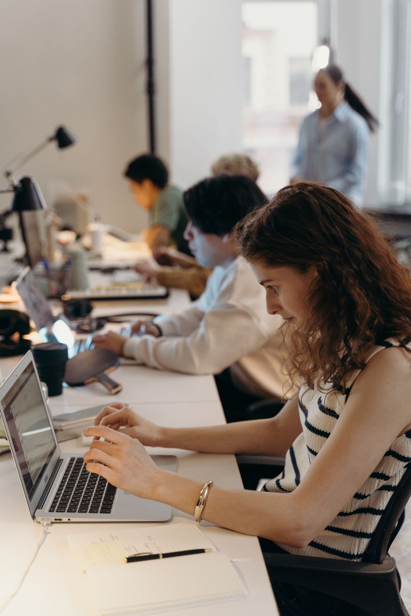 People working with laptops and notebooks at a shared desk in a bright workspace